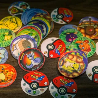 A scatter of Pokémon Tazos and Poké Ball slammers
