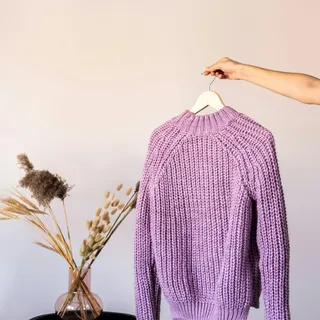 A purple knit sweater held up on a hanger